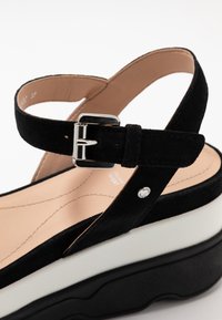 Sandali wedge neri in suede con cinturino alla caviglia, hardware in metallo argento, suola intermedia bianca e suola esterna nera testurizzata.