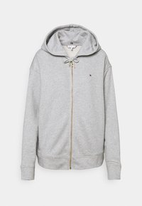 Sudadera gris con cremallera hecha de algodón suave, con capucha ajustable mediante cordones, puños acanalados y un pequeño logotipo bordado en el pecho.