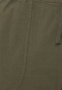 Gros plan d’un tissu vert olive avec une couture visible et une extrémité de cordon tricotée sur le côté droit.