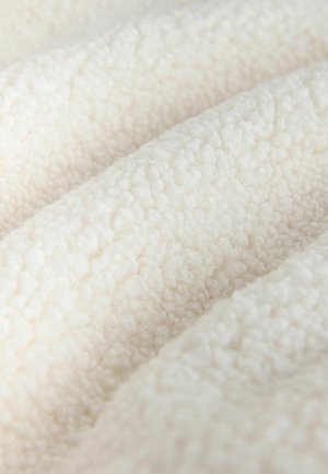 Texturált, puha fehér szövet, puha, bolyhos felülettel; sima fürtök és hurkok barátságos megjelenést és tapintható lágy érzetet kölcsönöznek.