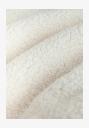 Texturált, puha fehér szövet, puha, bolyhos felülettel; sima fürtök és hurkok barátságos megjelenést és tapintható lágy érzetet kölcsönöznek.