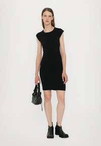 Rochie neagră fără mâneci, cu o siluetă ajustată, realizată dintr-un material elastic. Asortată cu o geantă mică, cu cuișoare, și bocanci negri până la gleznă.
