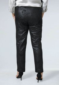 Zwarte nepleer broek met een glanzende textuur, met een slim fit en subtiele patronen. Gecombineerd met zwarte hoge hakken.