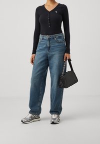 Sort langærmet bodysuit med knaplukning ved halsen, lyseblå denim wide-leg jeans, sølv sneakers og en lille sort håndtaske.