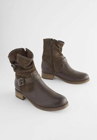 Bottines marron en cuir lisse et en daim, avec un design lâche, un détail de boucle ajustable et un petit talon en bois.