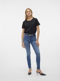 Svarte bomull T-skjorte kombinert med blå smale jeans. Modellen har på seg spisse svarte hæler. Enkelt design med en fitted silhuett og beltedetalj.