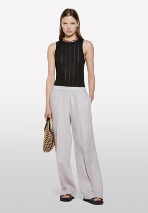 Haut sans manches noir avec des rayures verticales, associé à un pantalon large gris clair. Accessoire comprenant un sac en toile avec une finition texturée.