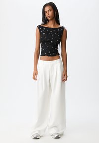 Zwarte getailleerde top met ronde zilveren accenten; gecombineerd met losse witte broeken en zilveren sneakers. Glad stof, casual stijl.