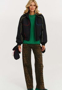Čierna krátka bomber bunda s farebným lemovaním, skombinovaná so zeleným sveterom a nohavicami s leopardím vzorom. Doplnené čiernymi rukavicami.