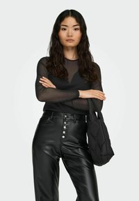 Black sheer long-sleeve top, high-neck design; paired with high-waisted black faux leather pants featuring front buttons. Holds a quilted black bag.