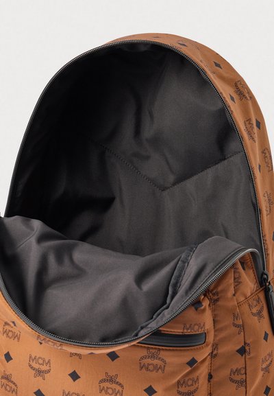 Sac à dos marron avec un motif de logo, fermeture à zip et doublure intérieure noire. Le tissu a une texture lisse et une forme structurée.