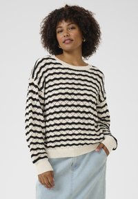 Pull en tricot avec un motif de vagues en noir et crème, à coupe décontractée, col large, et poignets et ourlet côtelés.