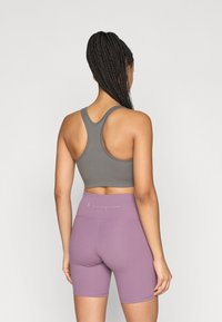 Γκρι αθλητικό τοπ χωρίς μανίκια και μωβ ποδηλατικά σορτς, εφαρμοστά, με ραφές λεπτομέρειες. Το λογότυπο είναι διακριτικά ορατό στη μέση των σορτς.