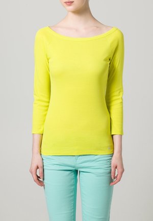 Geel, top met driekwartmouwen en een bootnek, met een gladde textuur. Gecombineerd met mintgroene, strakke broek.