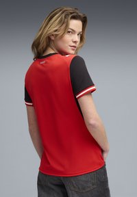 Ανδρικό κόκκινο αθλητικό πουκάμισο με μαύρα κοντά μανίκια, διαθέτει στρογγυλή λαιμόκοψη, ριγέ λεπτομέρεια κοντά στις μανσέτες και διακριτικό λογότυπο στο πίσω μέρος.