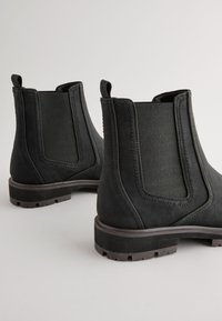 Schwarze Stiefeletten mit strukturierten elastischen Einsätzen, rundem Zehenbereich und robusten Gummisohlen. Mit Laschen zum einfachen An- und Ausziehen.