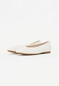 Des chaussures blanches à semelle plate avec une tige synthétique lisse, un petit talon et une conception à bout arrondi. Accentué avec une semelle contrastante de couleur brun clair.