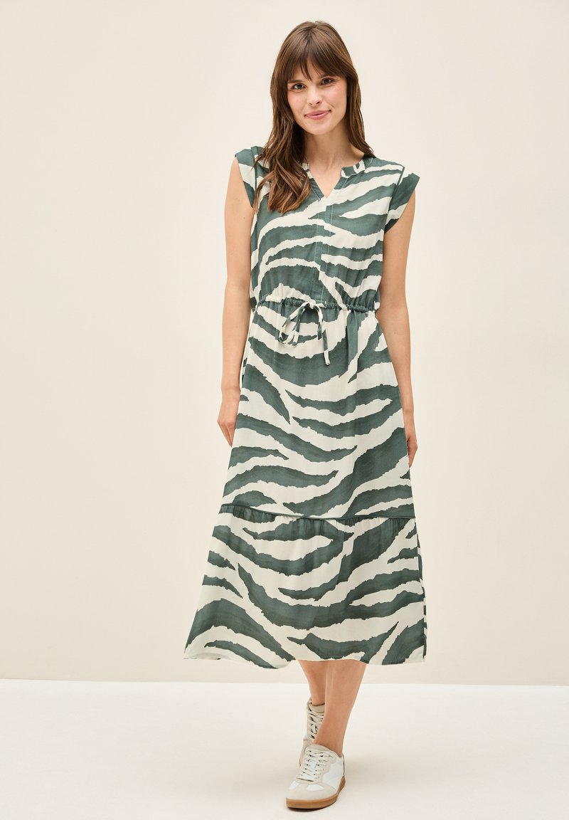 Vihreä-valkoinen raidallinen midimekko, jossa on lyhyet hihat, V-pääntie ja säädettävä vyötärön naru. Yhdistetty valkoisiin tennareihin.