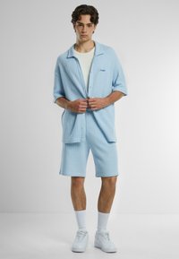 Light blue knitted short-sleeve shirt with pocket, white T-shirt underneath, matching knee-length shorts, and white sneakers.