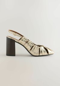 Gold metallic leather slingback shoe with wide block heel and strappy cut-out design on toe and sides, side view on light background.