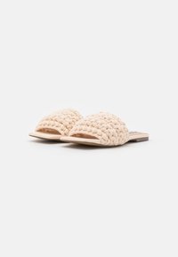 Sandali slide beige intrecciati con punta arrotondata, aperti davanti, suola piatta e superficie texturizzata. Design minimalista senza ulteriori decorazioni.