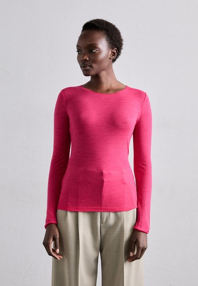 Maglietta a maniche lunghe di un brillante colore rosa, con scollatura rotonda, realizzata in tessuto testurizzato, abbinata a pantaloni beige a gamba larga.