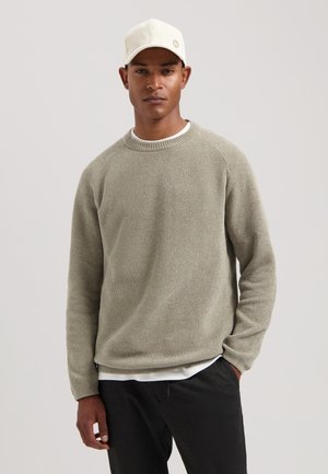 Light green knit sweater with a textured pattern, round neck, and long sleeves, paired with a white undershirt and dark pants.