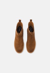 Bottes chelsea en daim marron avec un bout arrondi, des panneaux élastiques sur les côtés et des languettes pour faciliter l'enfilage, dotées d'une semelle texturée pour une meilleure adhérence.