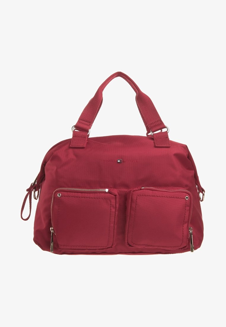 Punainen nailonihandbag, jossa on kaksinkertaiset vetoketjulliset etutaskut, tukevat yläkahvat ja helposti saavutettava pääosasto. Sujuva tekstuuri, suorakulmainen muoto.