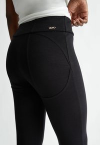 Svarta leggings med ett slätt, stretchigt tyg; hög midja; subtila sömnadsdetaljer; liten metall-logotyp nära midjan.