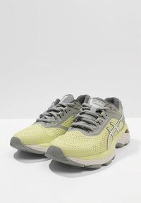 Baskets de course jaune clair avec des accents gris, tige en maille pour une respirabilité, semelle texturée et détails réfléchissants. Design à lacets.