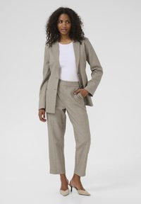 Costume taillé gris clair avec un pantalon droit ; tissu texturé ; blazer à un bouton ; associé à un haut blanc et des talons beiges.