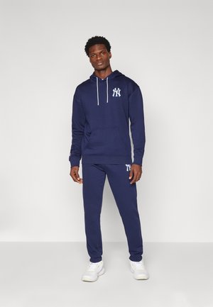 Navy blue hoodie with white logo on chest and drawstring, paired with matching navy joggers featuring logo on thigh. Smooth cotton texture.