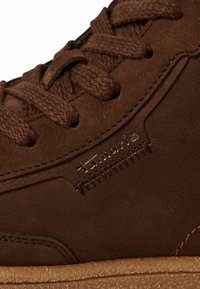 Gros plan sur une basket en cuir marron avec de gros lacets marron et le logo « Tamaris » brodé au-dessus de la semelle en caoutchouc texturée.