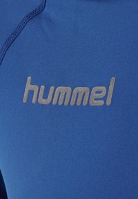 Blauer Sportbekleidungsstoff mit glatter Textur, rundem Hals und dem grauen "hummel"-Logo auf der Brust.
