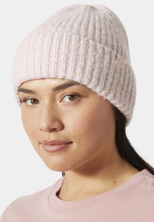 Mujer con gorro de punto rosa claro y camiseta rosa claro a juego, mirando ligeramente hacia un lado sobre un fondo claro y sencillo.