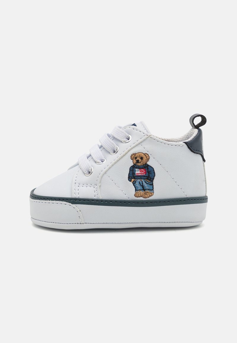 Λευκό δερμάτινο αθλητικό παπούτσι με γκρι λεπτομέρειες, σχέδιο με κορδόνια, και κεντητός αρκούδος σε μπλε ρούχα που κρατά μια αμερικανική σημαία στο πλάι.