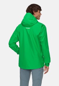 Grön vattentät jacka med huva, som har en slank design och elastiska ärmslut. Märkbart logotyp på övre ryggen.
