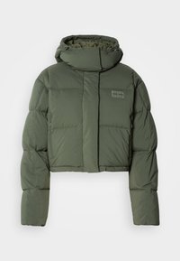 Veste matelassée raccourcie, olive, avec un col montant et des poches zippées. Elle présente un design matelassé et un logo discret sur le devant.