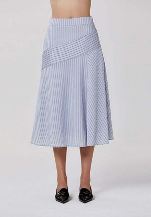 Jupe midi bleu clair avec fines rayures verticales et panneau diagonal, portée avec des mocassins noirs pointus, vue de la taille aux pieds.