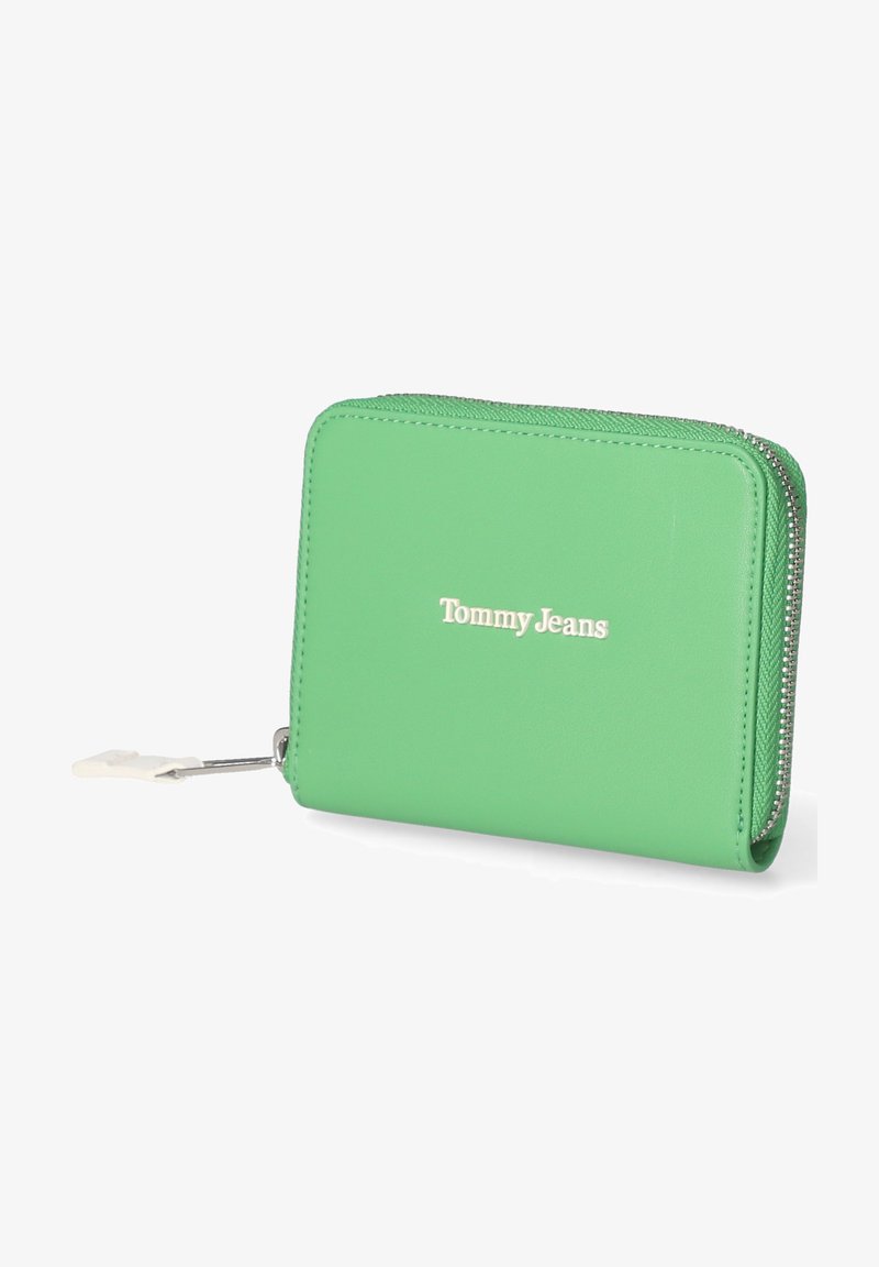 Portefeuille vert en simili cuir avec fermeture éclair, arborant un logo "Tommy Jeans" blanc à l'avant et des coutures texturées le long des bords.