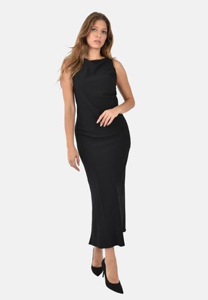 Abito nero senza maniche con una silhouette aderente, orlo a lunghezza ginocchio e tessuto liscio. Indossato con scarpe nere con tacco alto. Sfondo neutro.