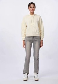 Sudadera con capucha de color amarillo claro y mangas texturizadas, con ribete en el dobladillo, combinada con jeans de campana grises y zapatillas blancas.