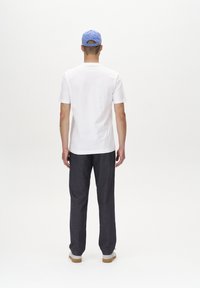 T-shirt bianco a maniche corte e pantaloni grigio scuro. Indossa un cappellino azzurro chiaro. L'outfit presenta una vestibilità rilassata e una texture morbida.