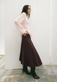 Suéter de lana rosa claro, falda plisada larga burdeos y botas negras de tacón alto. Se destacan texturas suaves y líneas elegantes.