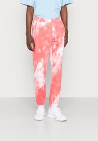 Rosa tie-dye sweatpants med elastisk midja, elastiska manschetter och avslappnad passform, i kombination med vita träningsskor.