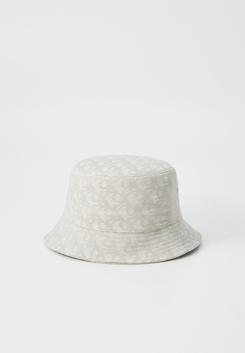Lys beige bøttehatt med et teksturert mønster, med en rund krone og bred, nedoverhellende brem. To ventilasjonsåpninger på siden.