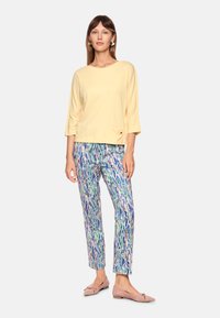 Light yellow three-quarter sleeve top with a pocket, paired with colorful patterned trousers featuring blue, green, and pink hues. Beige flats.