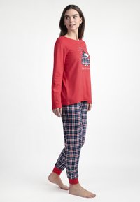 Camisón rojo de manga larga con un gráfico temático de nieve, combinado con pantalones de cuadros en tonos marino y rojo con puños acanalados rojos. Material suave de algodón.