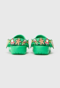 Tamancos verdes brilhantes com charms de Natal, incluindo o Pai Natal, homem de gengibre, bengala de carinho e azevinho nas tiras de calcanhar ajustáveis.